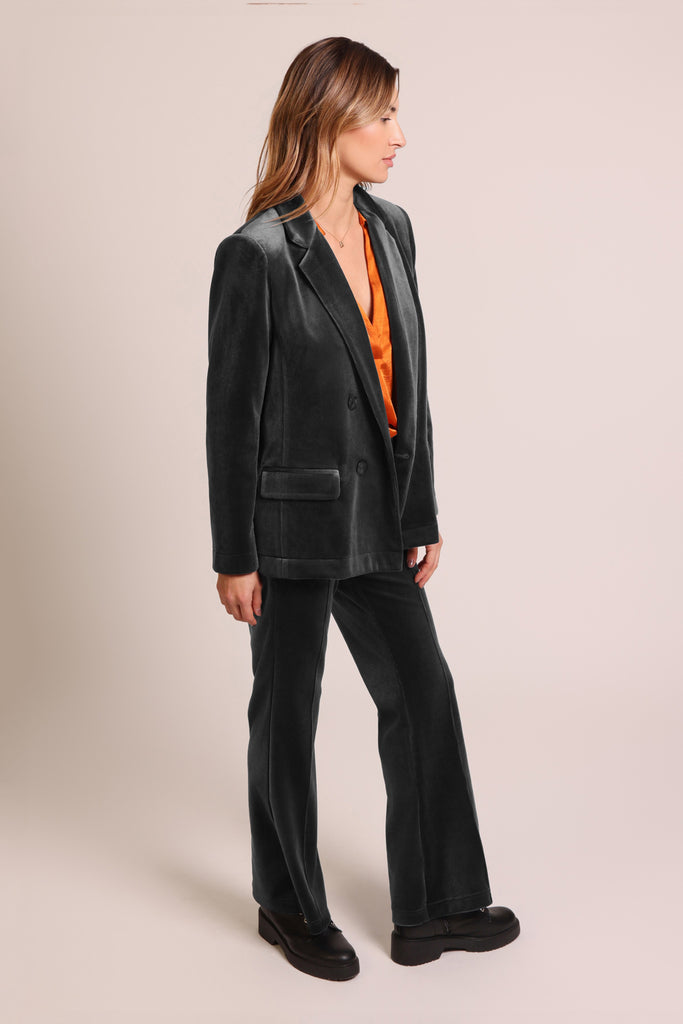 Side shot of model wearing black cord velvet long sleeve button front blazer jacket.