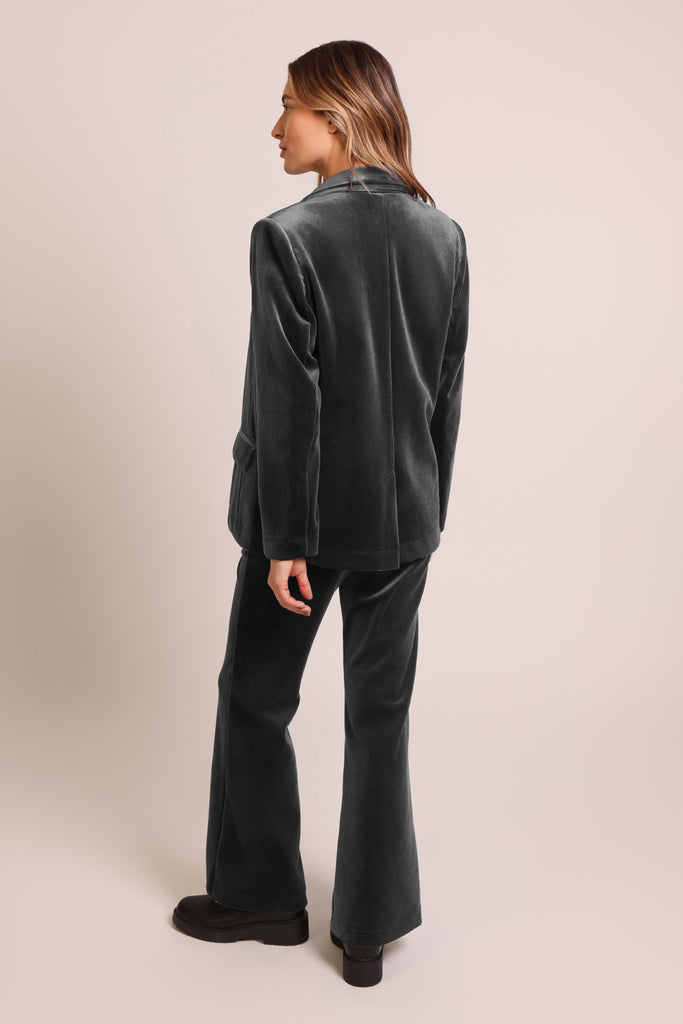 Back shot of model wearing black cord velvet long sleeve button front blazer jacket.