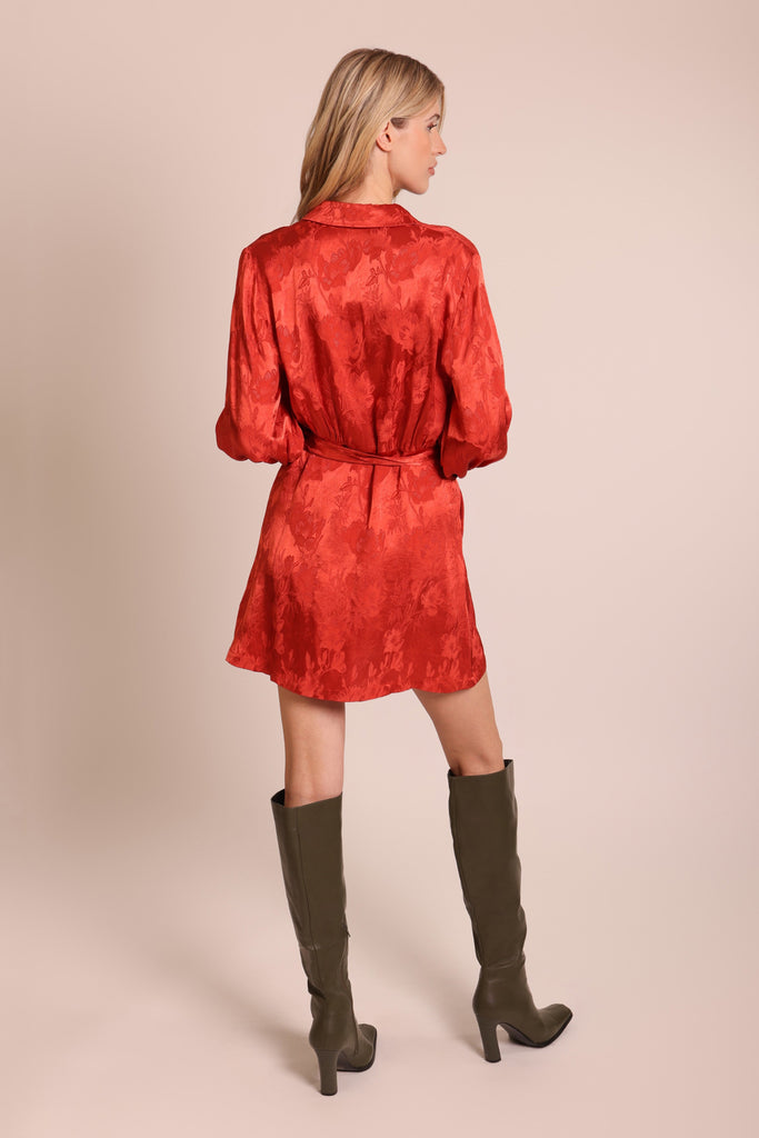 Back shot of a model wearing a rust red floral long sleeve tie waist mini shirt dress.