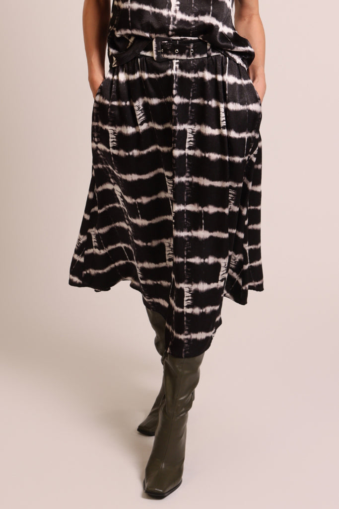 Close up front shot of model wearing a black and white brick wall print belted midi skirt with pockets.