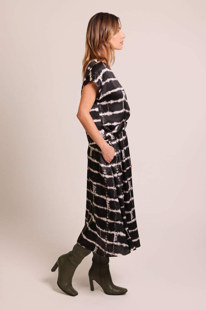 Side shot of model wearing a black and white brick wall print belted midi skirt with pockets.