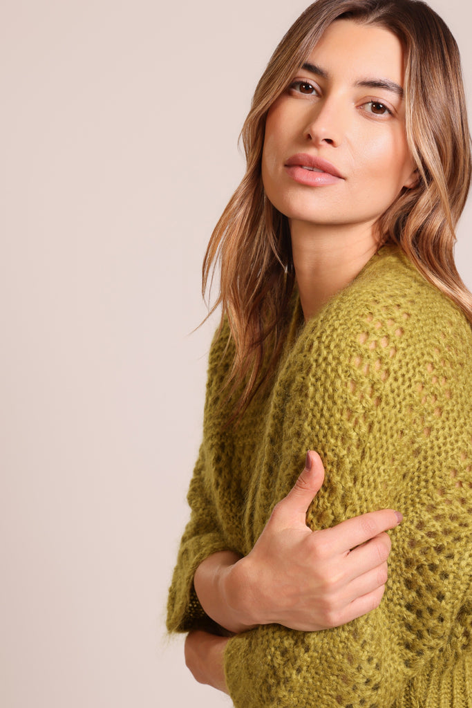 Close up side shot of model wearing a knitted green three quarter sleeve unfastened cardigan.