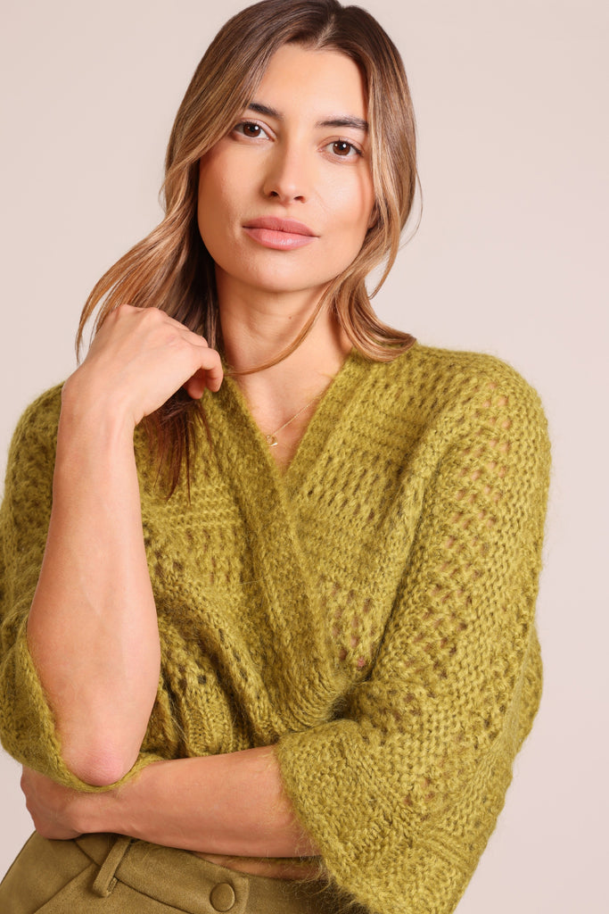 Close up front shot of model wearing a knitted green three quarter sleeve unfastened cardigan.