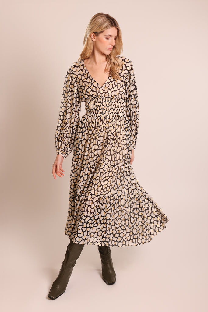 Front shot of model wearing a white black and gold print long sleeve elasticated waist tiered skirt midi dress.