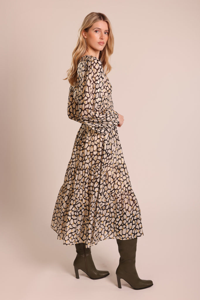 Side shot of model wearing a white black and gold print long sleeve elasticated waist tiered skirt midi dress.