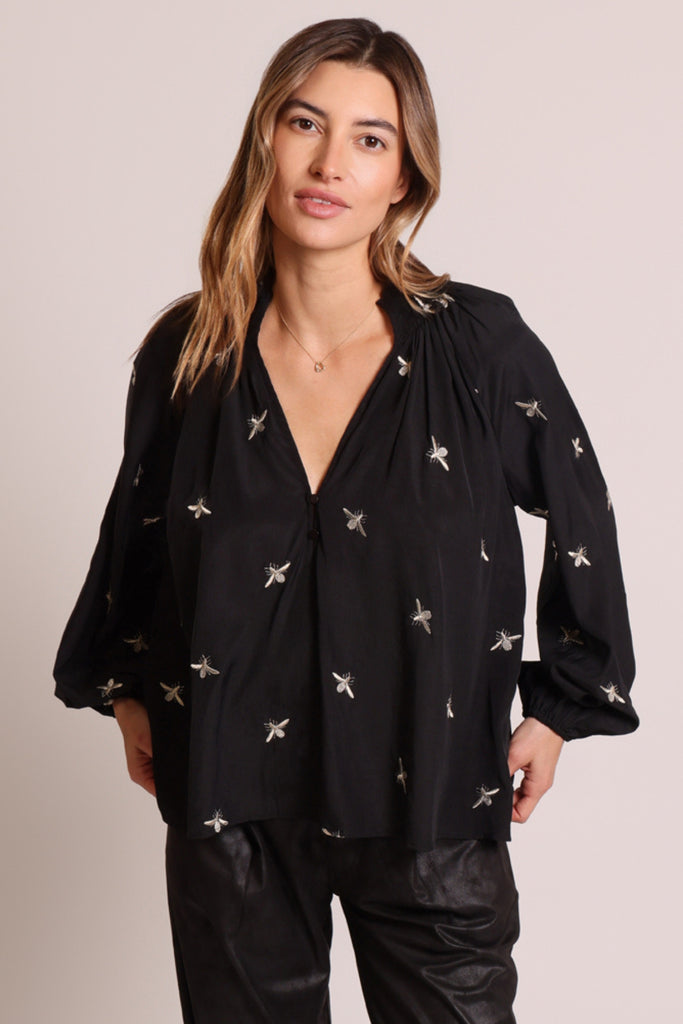 Close up front shot of model wearing a black long sleeve V-neck relaxed fit blouse with metallic bee embroideries.
