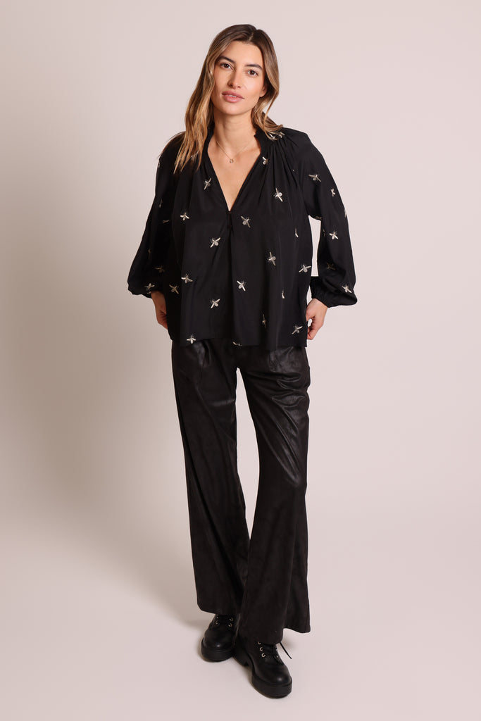 Front shot of model wearing a black long sleeve V-neck relaxed fit blouse with metallic bee embroideries.